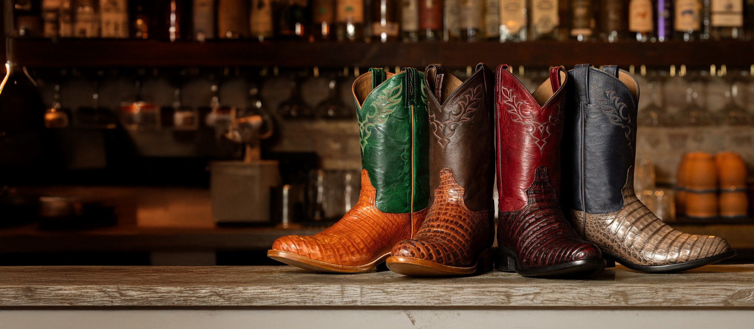 Una foto de abanico de las botas vaqueras Delmonte Caiman de 11” en varios colores frente a un bar.